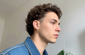 Jeune homme de profil avec une wolf cut bouclée, une veste en jean et une boucle d'oreille créole dorée.